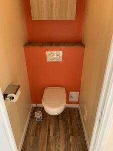 WC mural avec mur orange et sol bois rénové