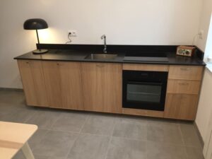 Cuisine aménagée installée avec meubles en bois, plan de travail foncé, évier, plaques et four encastré dans un intérieur rénové.